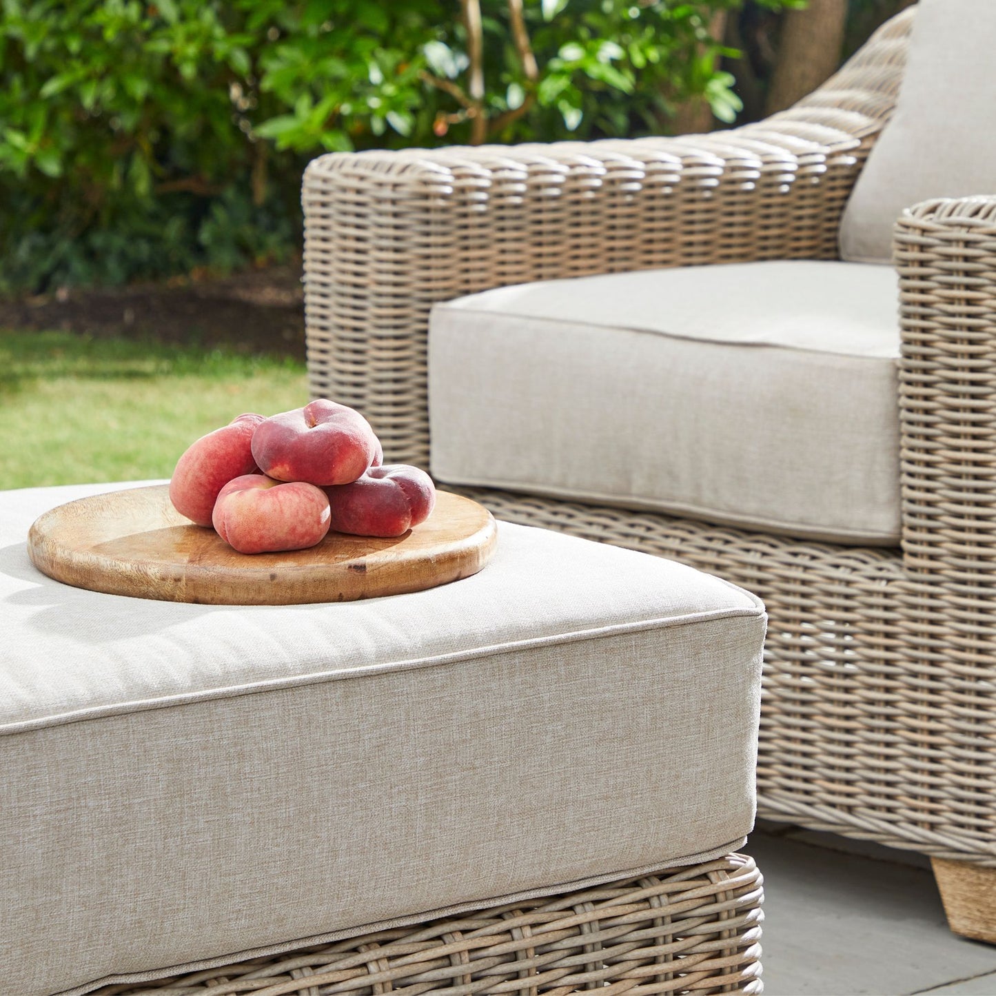 Peaches on a wooden cutting board on an outdoor ottoman with wicker furniture in the background.