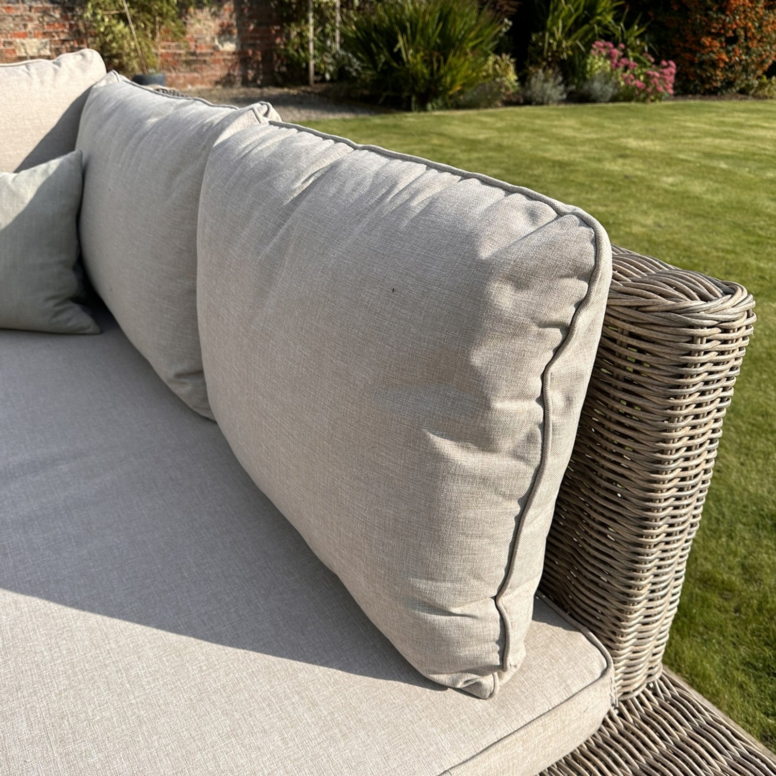 Gray cushions on a wicker outdoor sofa with a garden background