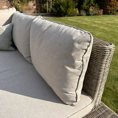 Gray cushions on a wicker outdoor sofa with a garden background