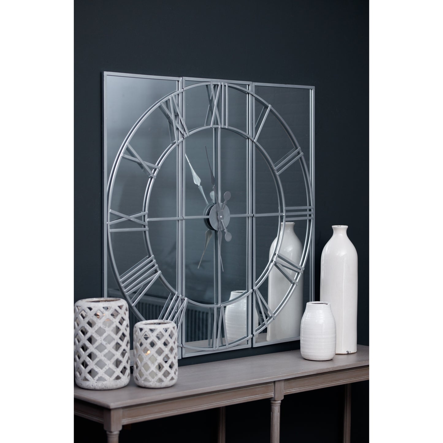 Decorative wall mirror with Roman numeral design on a dark wall with white vases.