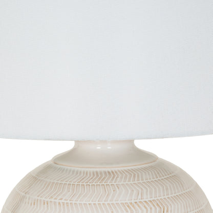 Close-up of a textured ceramic lamp base with a white lampshade on a light gray background