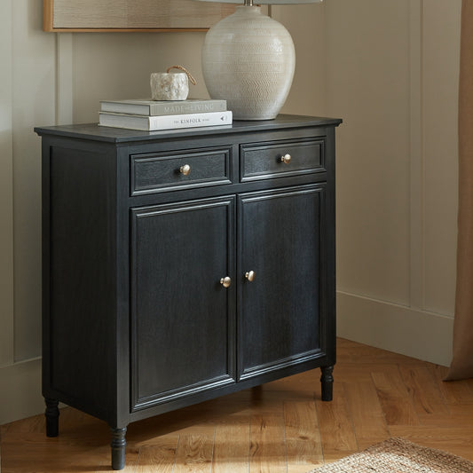 Black cabinet with two doors and two drawers on a wooden floor.