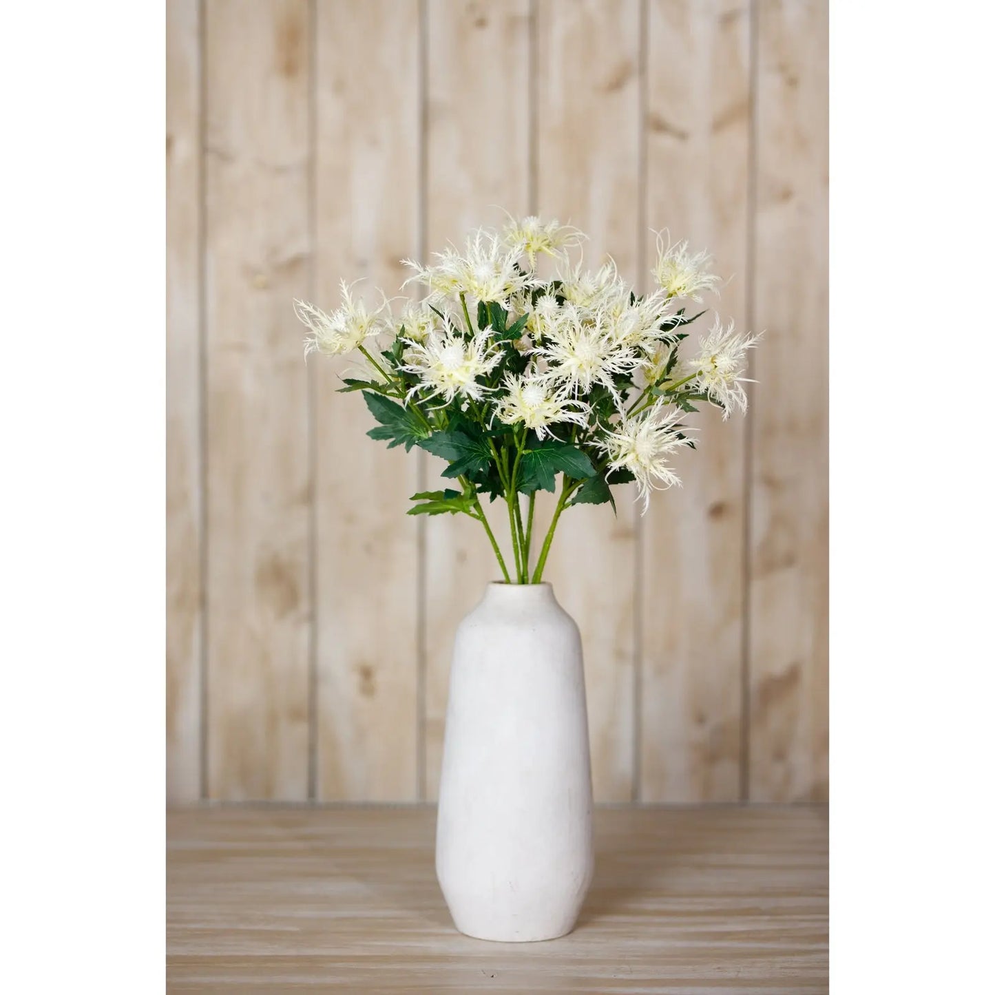 White vase with artificial flowers against a wooden panel background