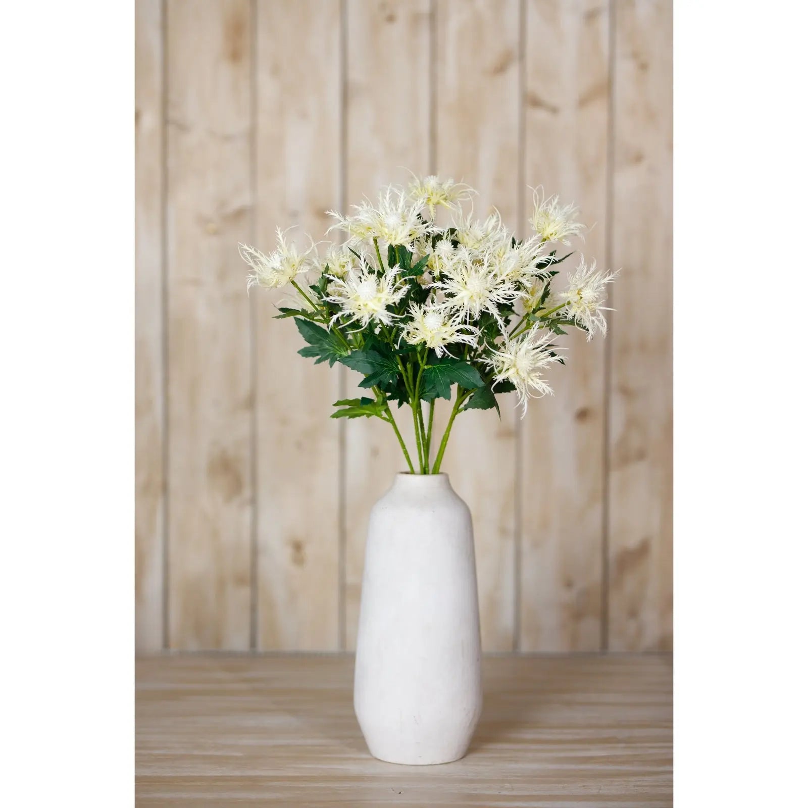 White vase with artificial flowers against a wooden panel background