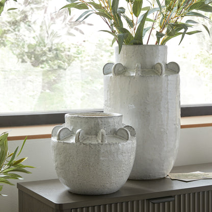 Two ceramic vases with handles on a windowsill with plants.