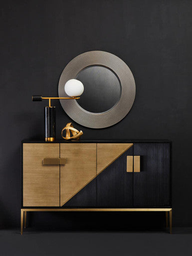 Modern cabinet with gold accents against a black wall with a round mirror.