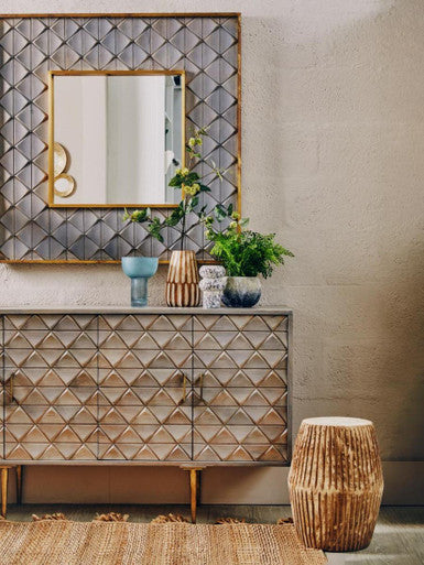 Decorative dresser with geometric pattern, mirror, and plants in a room.