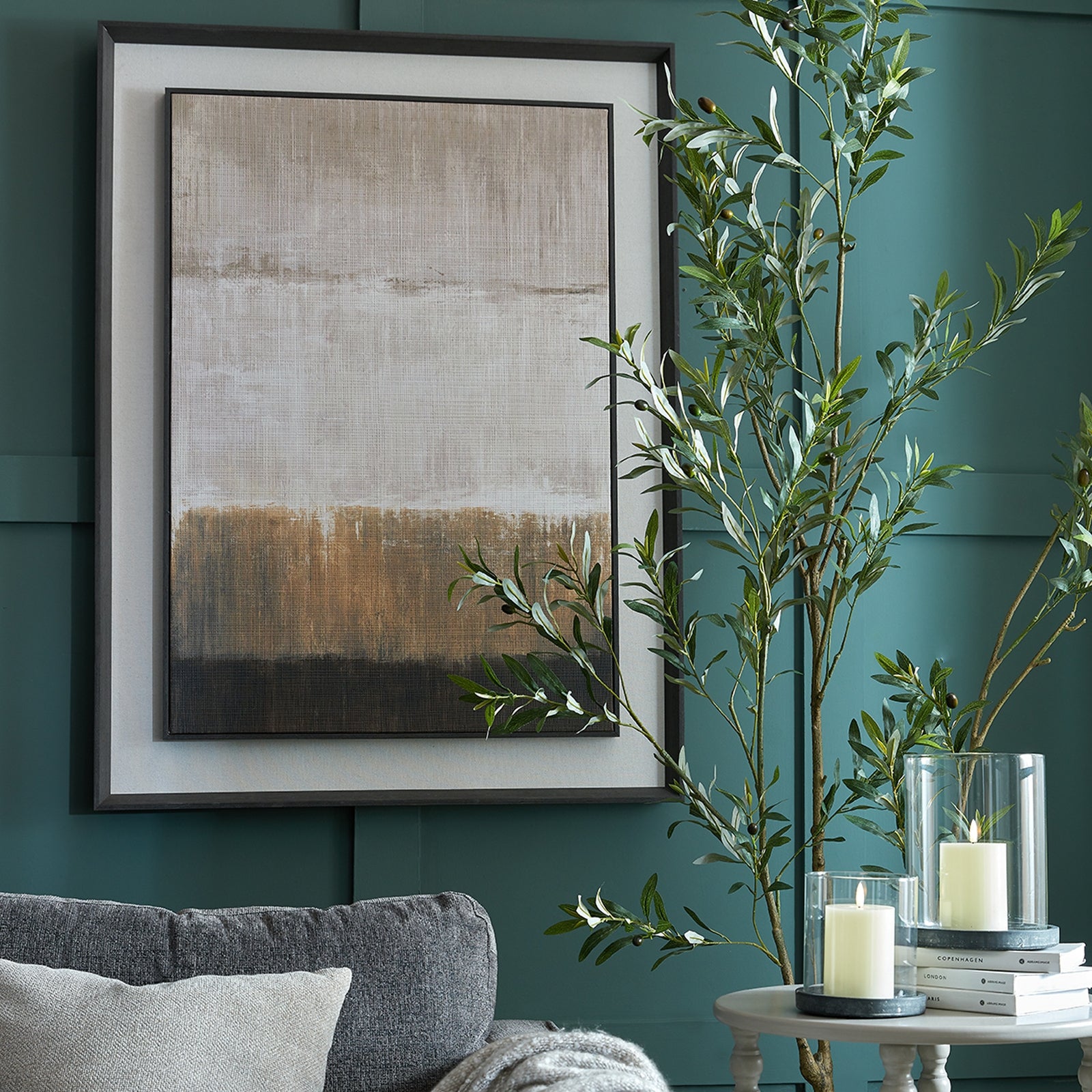 Framed abstract painting on a teal wall with a gray sofa and decorative items.