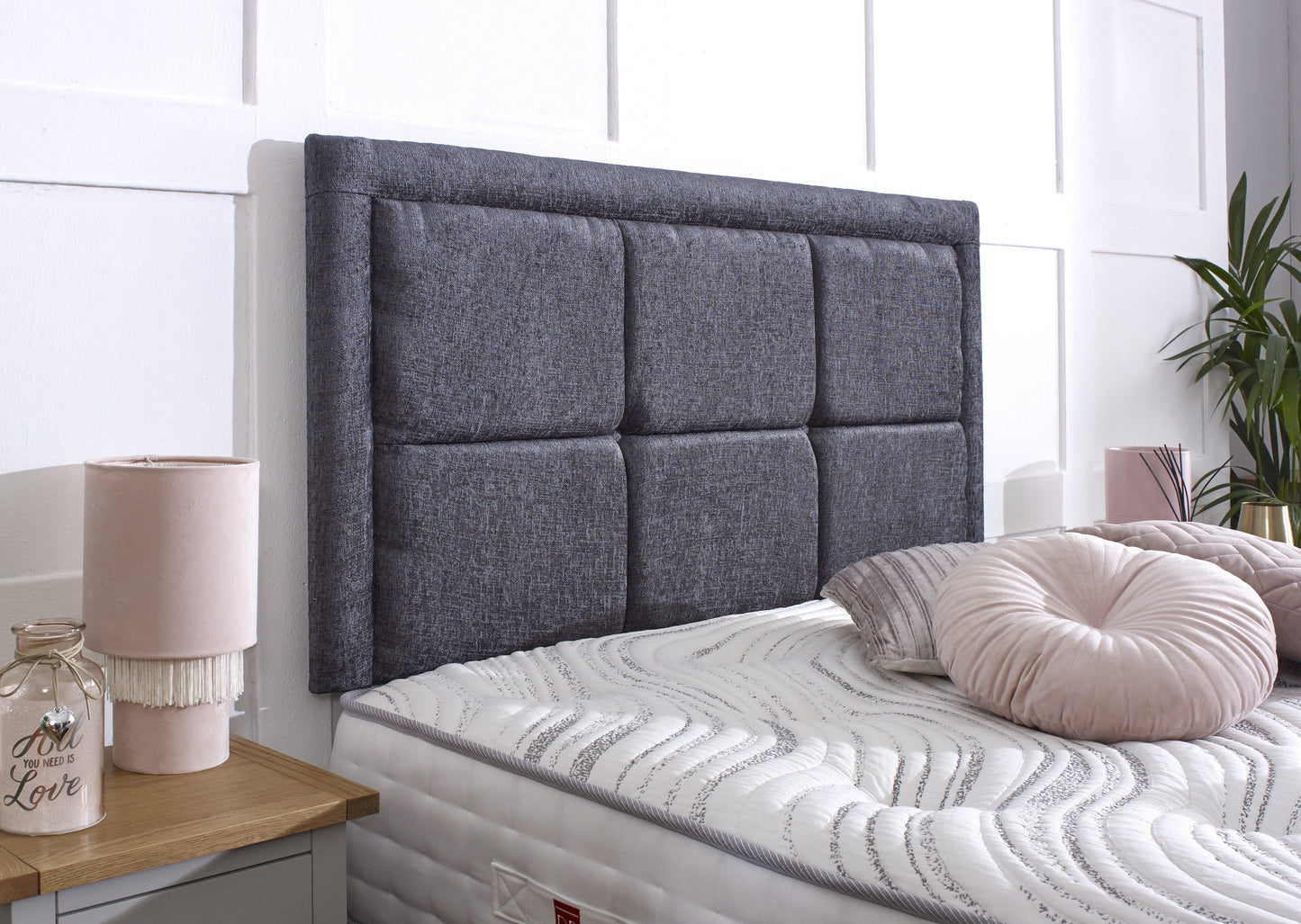 Gray upholstered headboard on a bed with pink pillows and a lamp in a bedroom setting.