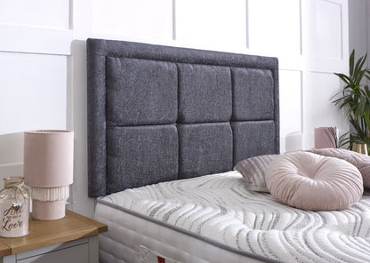 Gray upholstered headboard on a bed with pink pillows and a lamp in a bedroom setting.