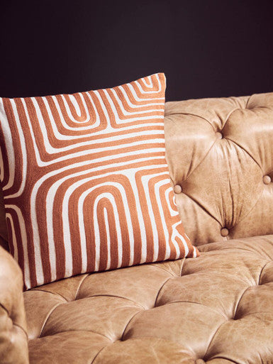 Decorative pillow with wavy pattern on a beige sofa against a black background