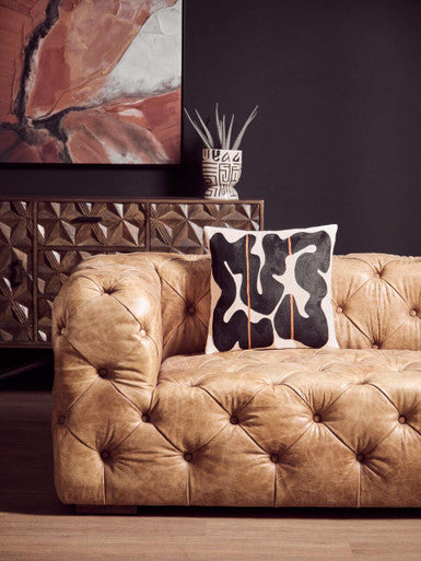 Brown tufted sofa with a decorative pillow in a living room setting.