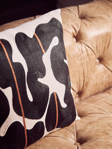 Decorative pillow with abstract black and white design on a brown tufted surface