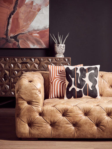 Brown tufted sofa with patterned cushions in a living room setting.