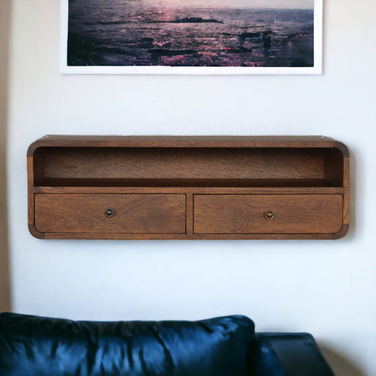 Wooden shelf with two drawers mounted on a wall above a black sofa.