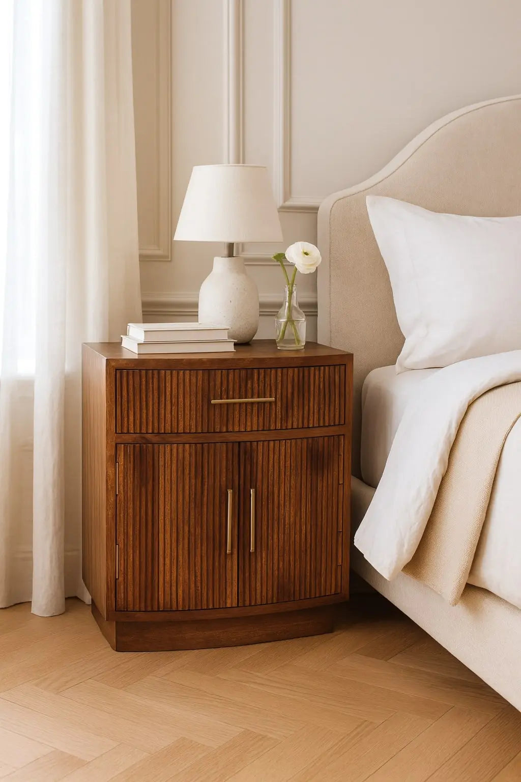 Wooden nightstand with lamp and books next to a bed in a bedroom setting