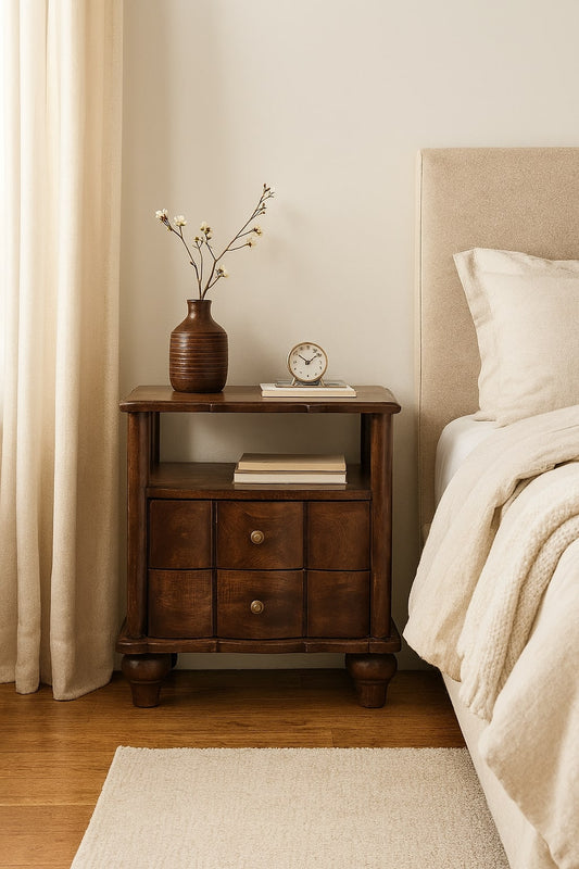 Wooden nightstand with decorative items next to a bed in a bedroom.