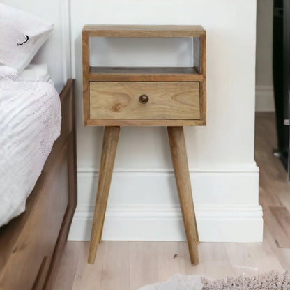 Wooden nightstand with a single drawer next to a bed in a bedroom.
