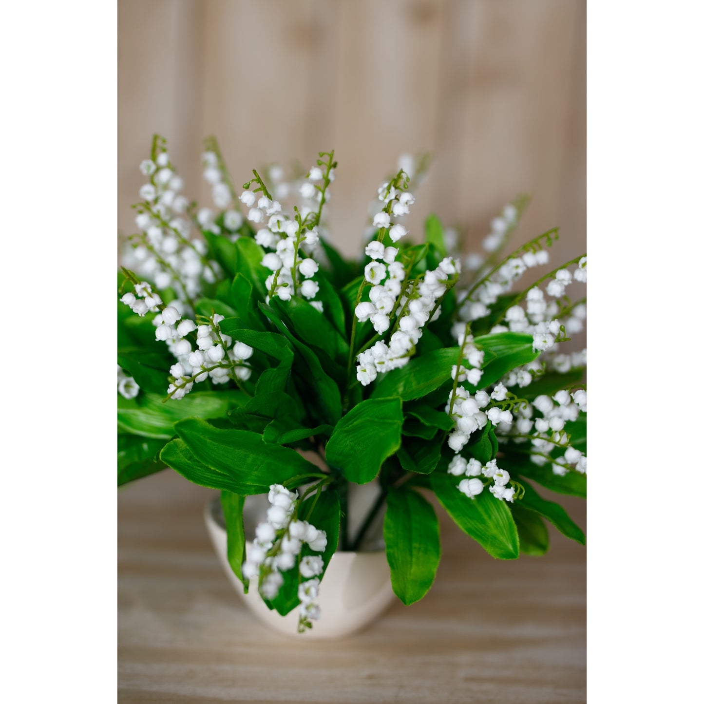 Bouquet of white flowers with green leaves in a white vase on a wooden surface.