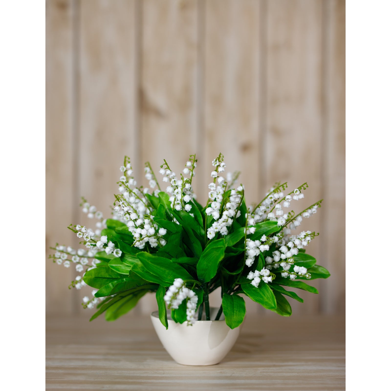 Bouquet of white flowers in a vase on a wooden surface with a wooden panel background