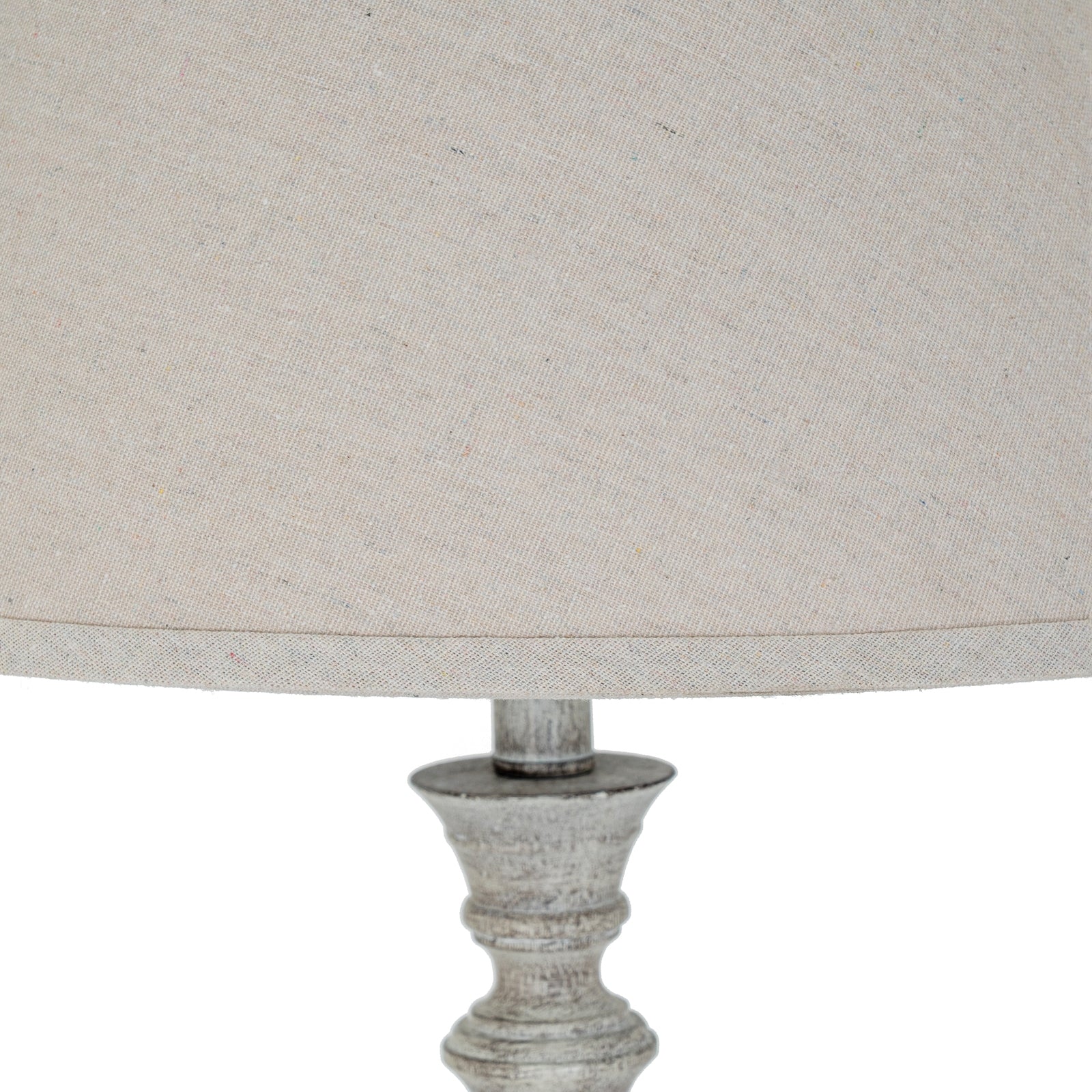 Close-up of a lamp with a textured base and beige fabric shade on a white background