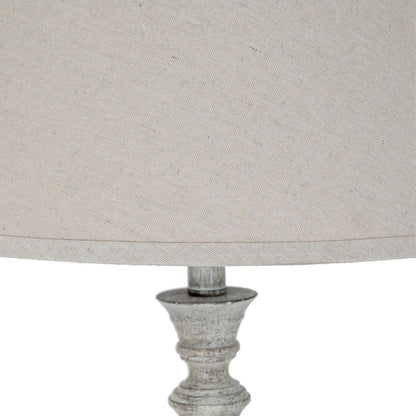 Close-up of a lamp with a textured base and beige fabric shade on a white background