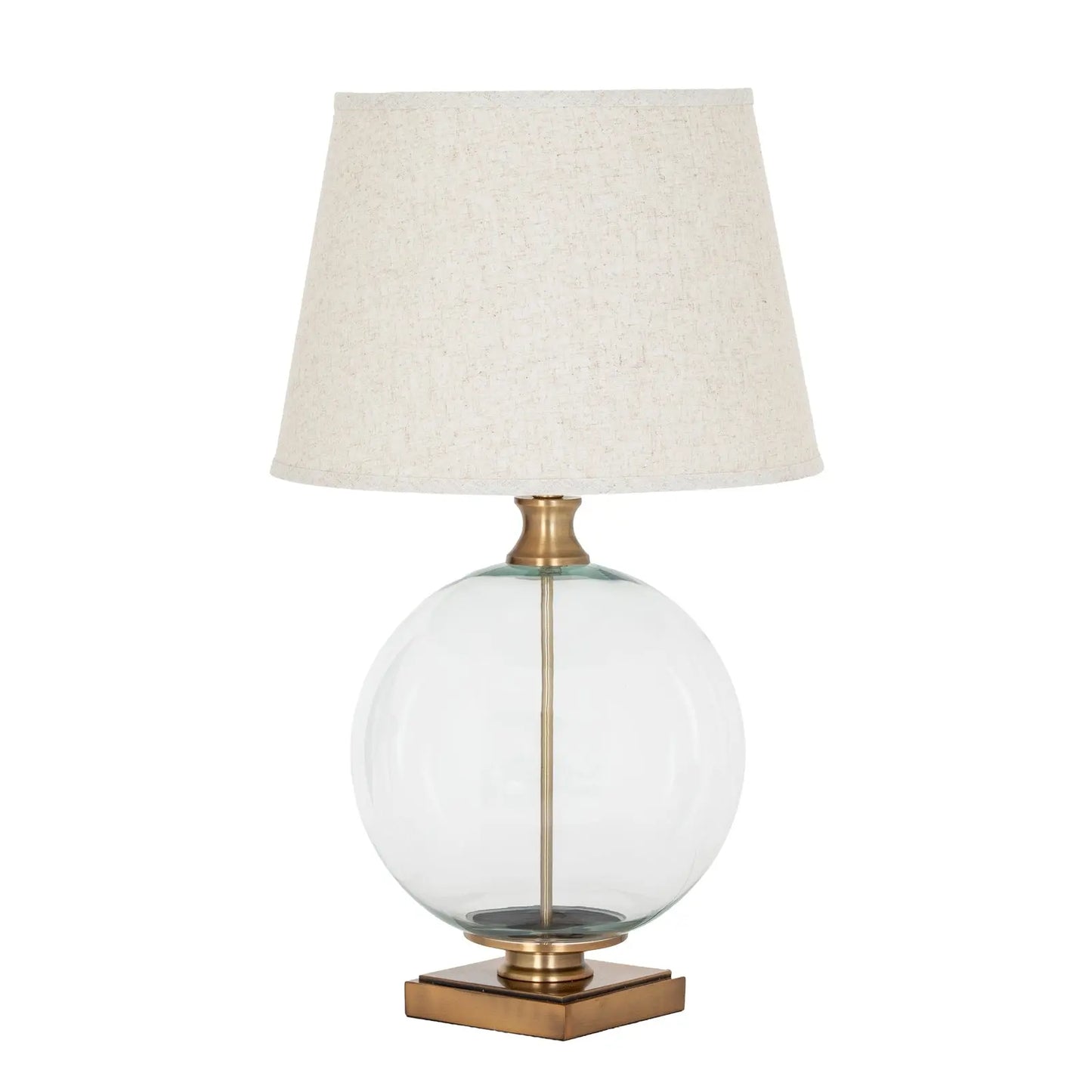 Table lamp with a clear glass base, brass accents, and a beige lampshade on a white background