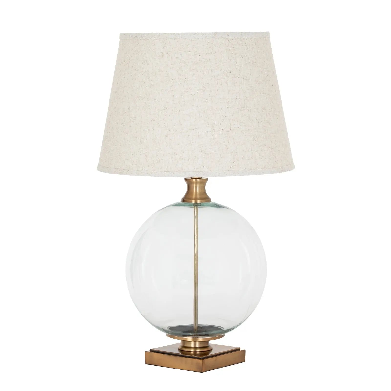 Table lamp with a clear glass base, brass accents, and a beige lampshade on a white background