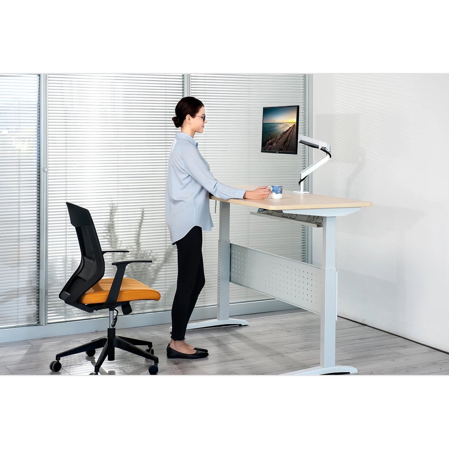 Person using a standing desk in an office setting with a chair and computer setup.