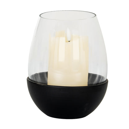 Clear glass candle holder with a black base containing a white candle on a white background