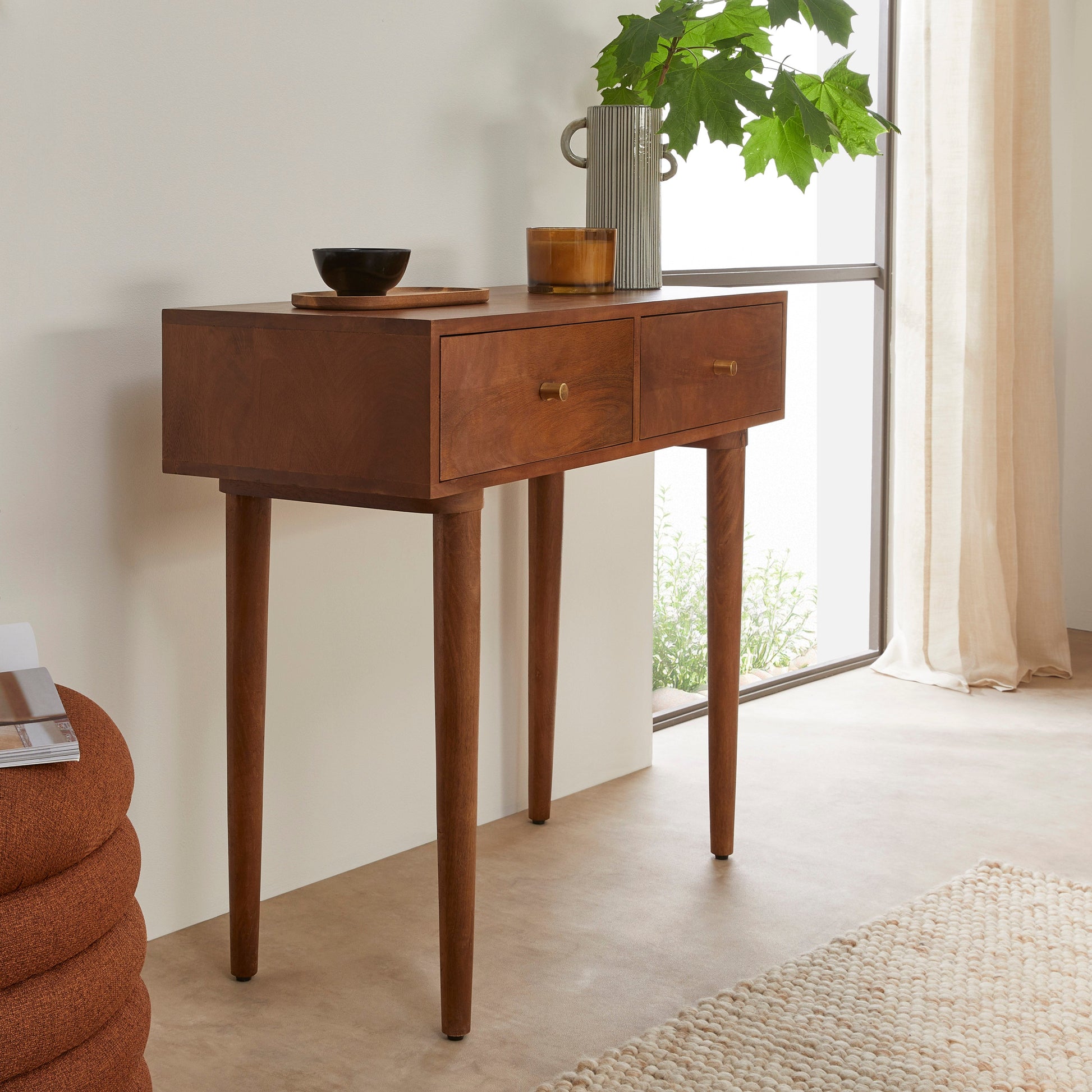 Wooden console table with decorative items in a room with a window and rug.