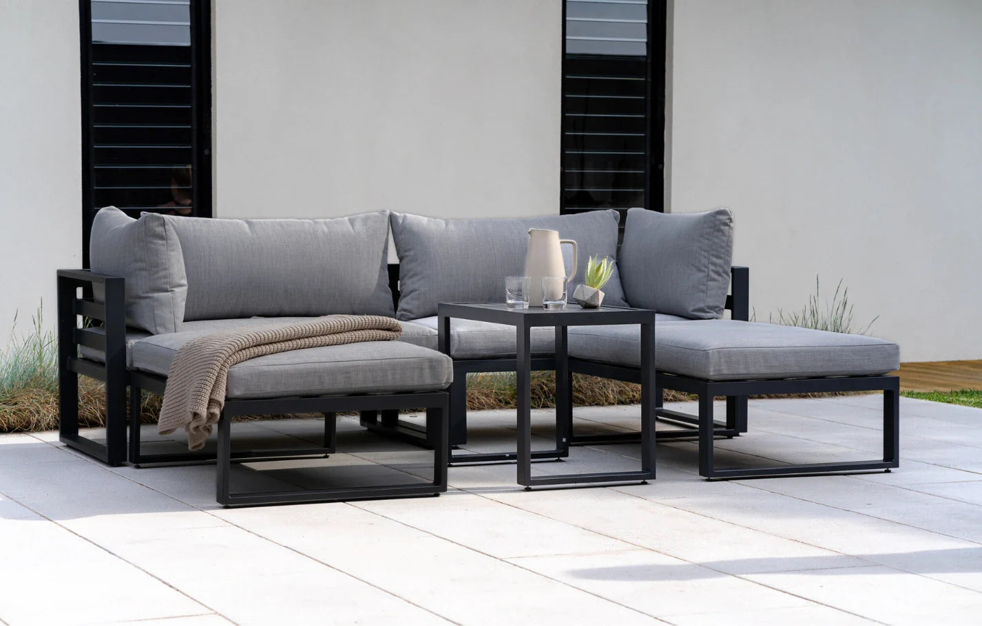 Outdoor patio furniture set with gray cushions and a small table on a patio.