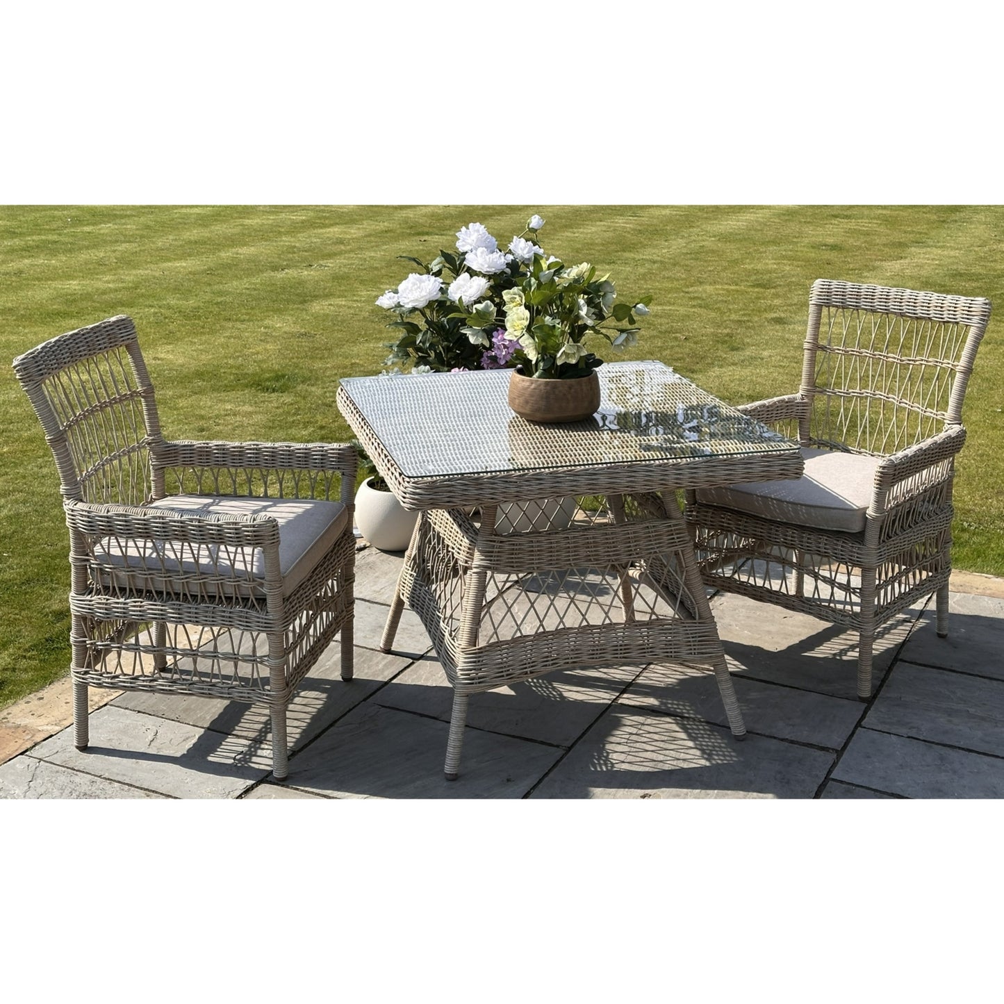 Outdoor patio set with wicker table and chairs on a patio with grass background
