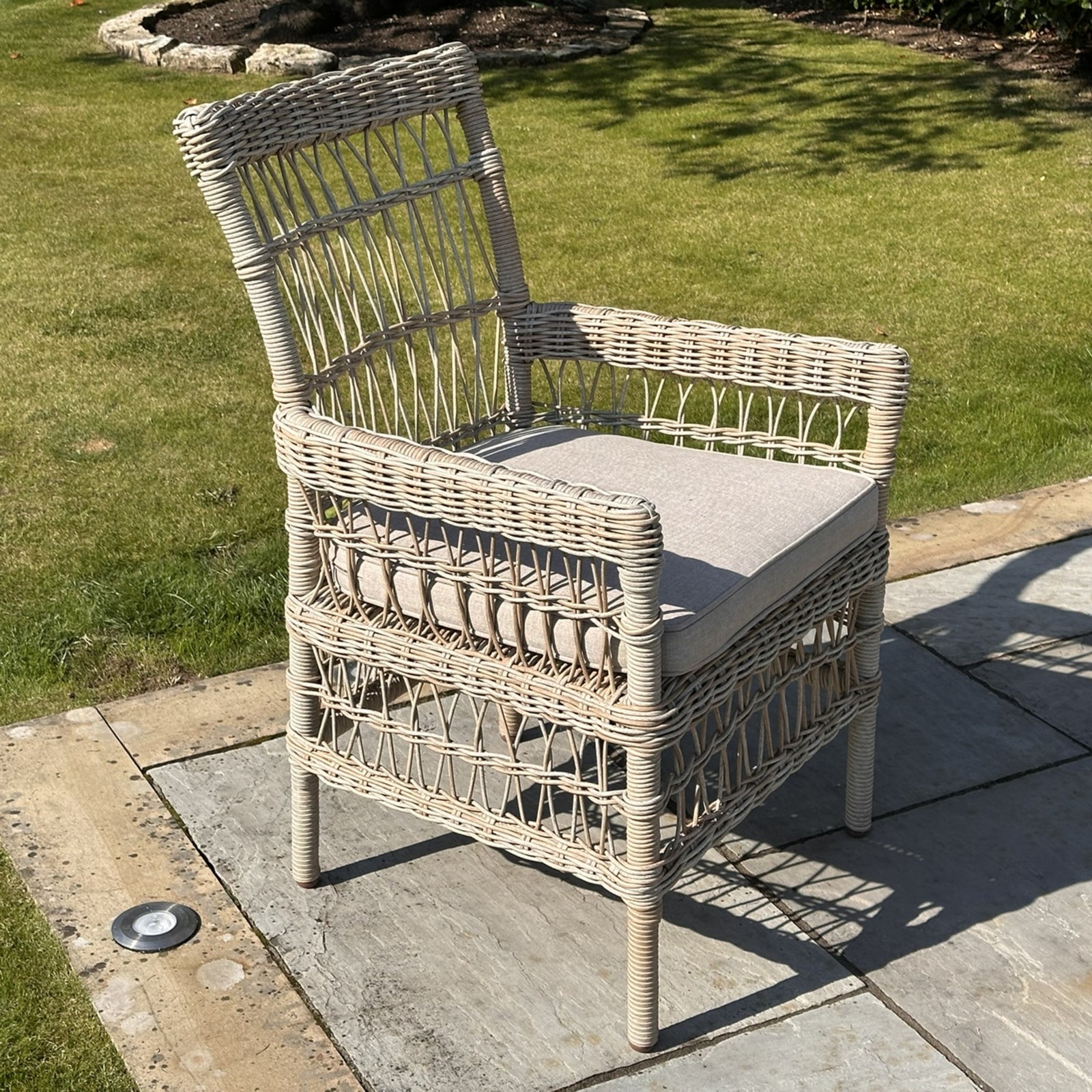 Wicker chair with a cushion on a patio area with grass in the background