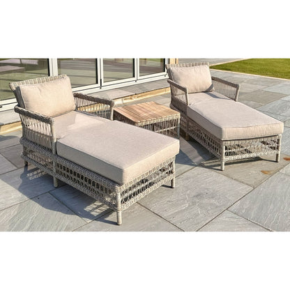 Two wicker outdoor lounge chairs with beige cushions on a stone patio.