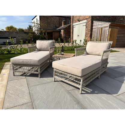 Two wicker outdoor lounge chairs with beige cushions on a stone patio.
