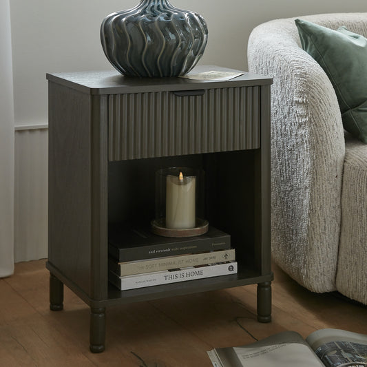 Dark wooden side table with a candle and books next to a beige sofa.