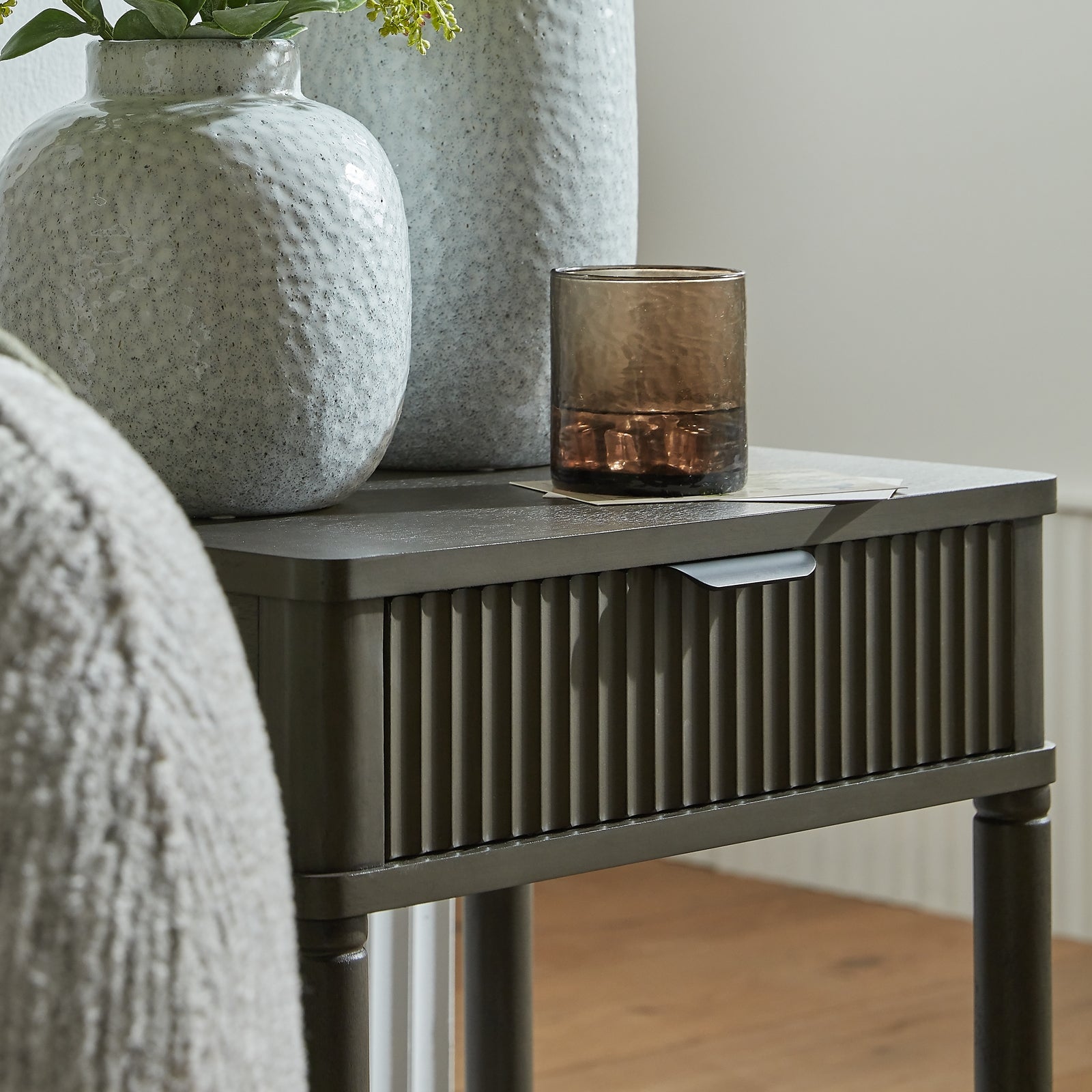 Side table with decorative items including a textured vase and a glass candle holder.