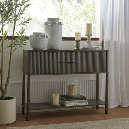 Console table with decorative items in a room with a plant and window.