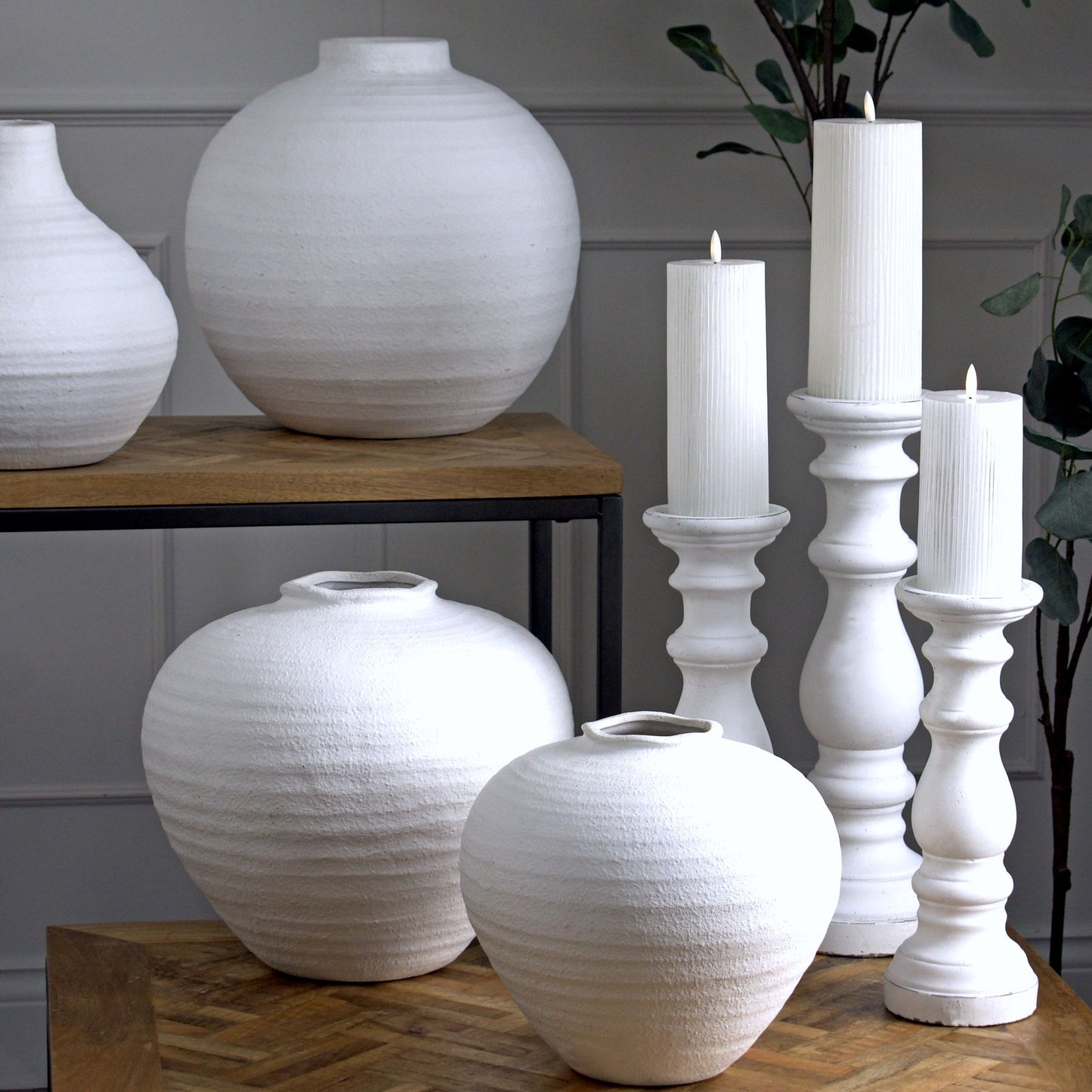 White ceramic vases and candle holders on a wooden surface with a neutral background