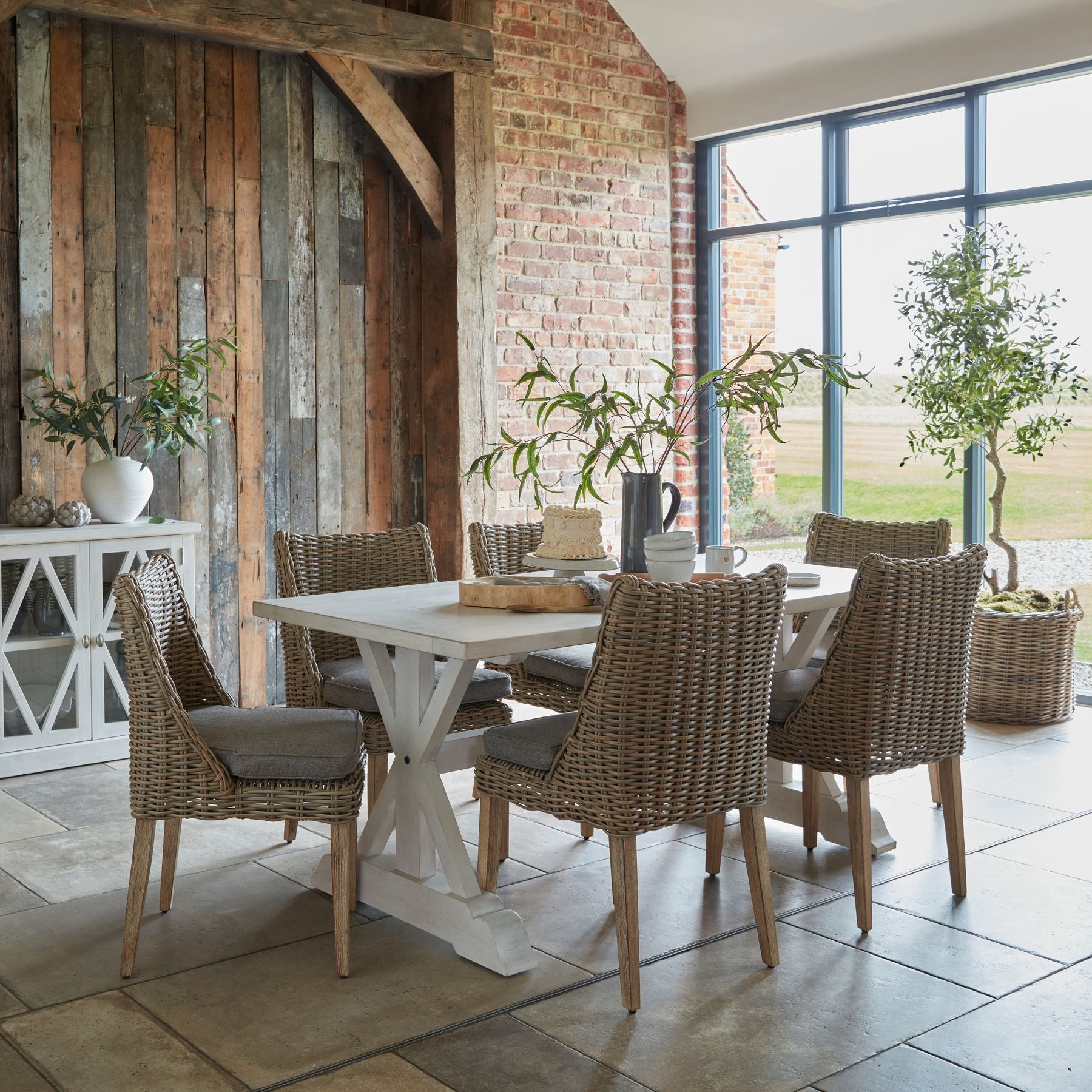 Dining area with a white table and wicker chairs in a rustic setting.