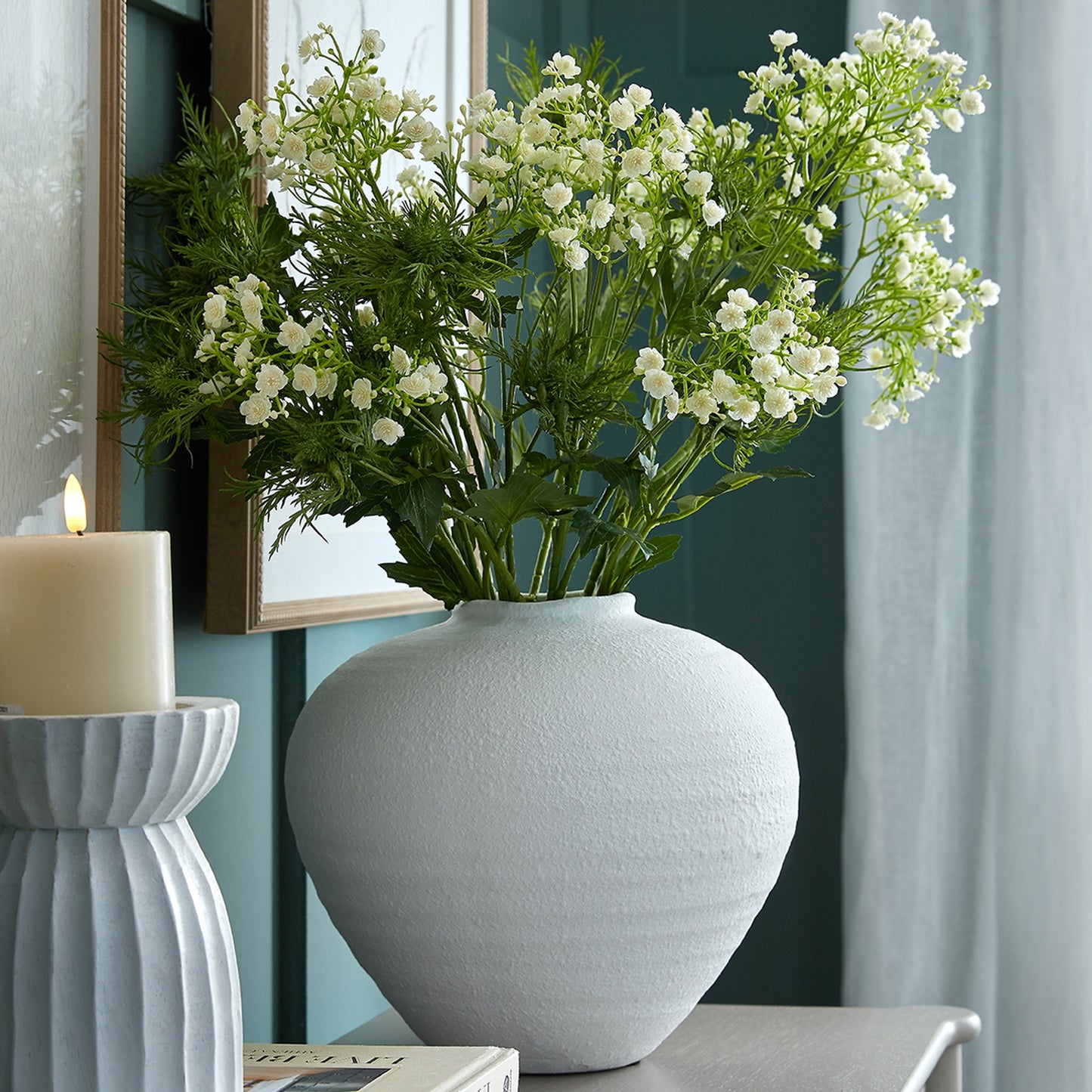 Gray vase with white flowers on a table next to a candle
