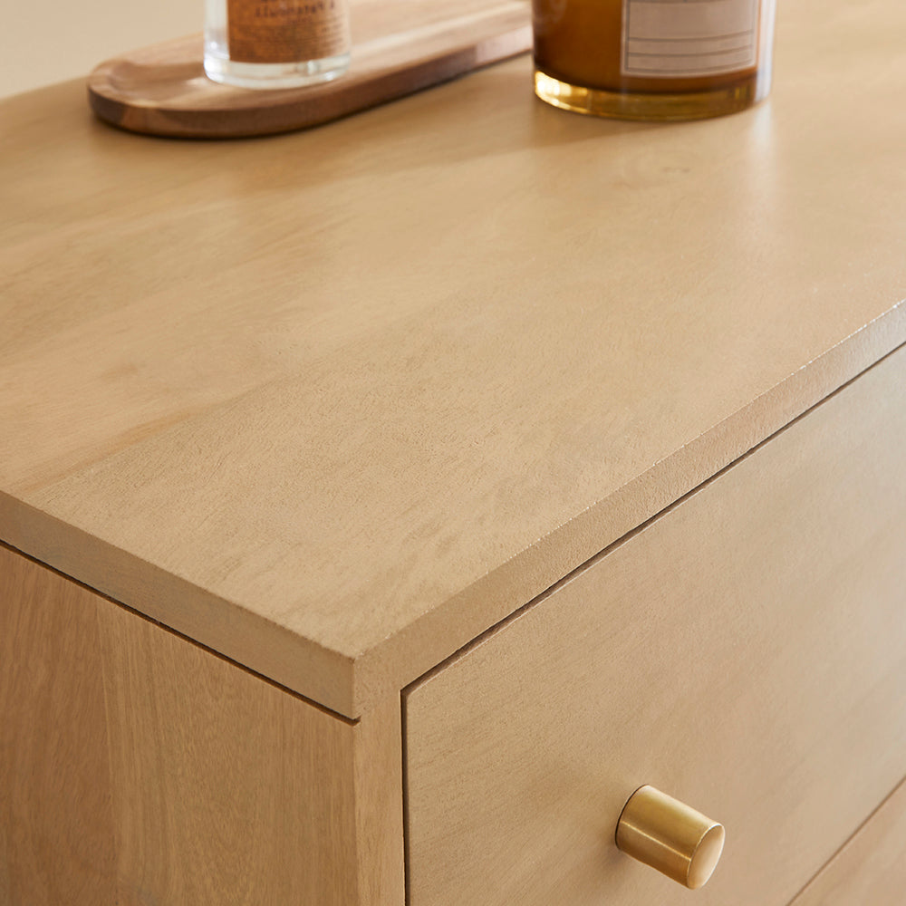 Close-up of a wooden drawer with a gold handle on a light wood surface.
