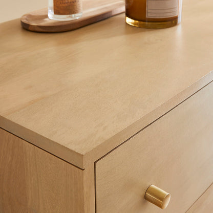 Close-up of a wooden drawer with a gold handle on a light wood surface.