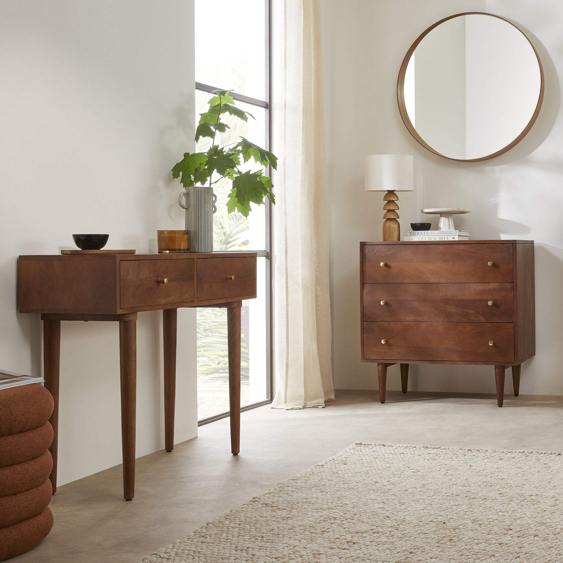 Wooden console table and dresser in a room with a large window and round mirror.