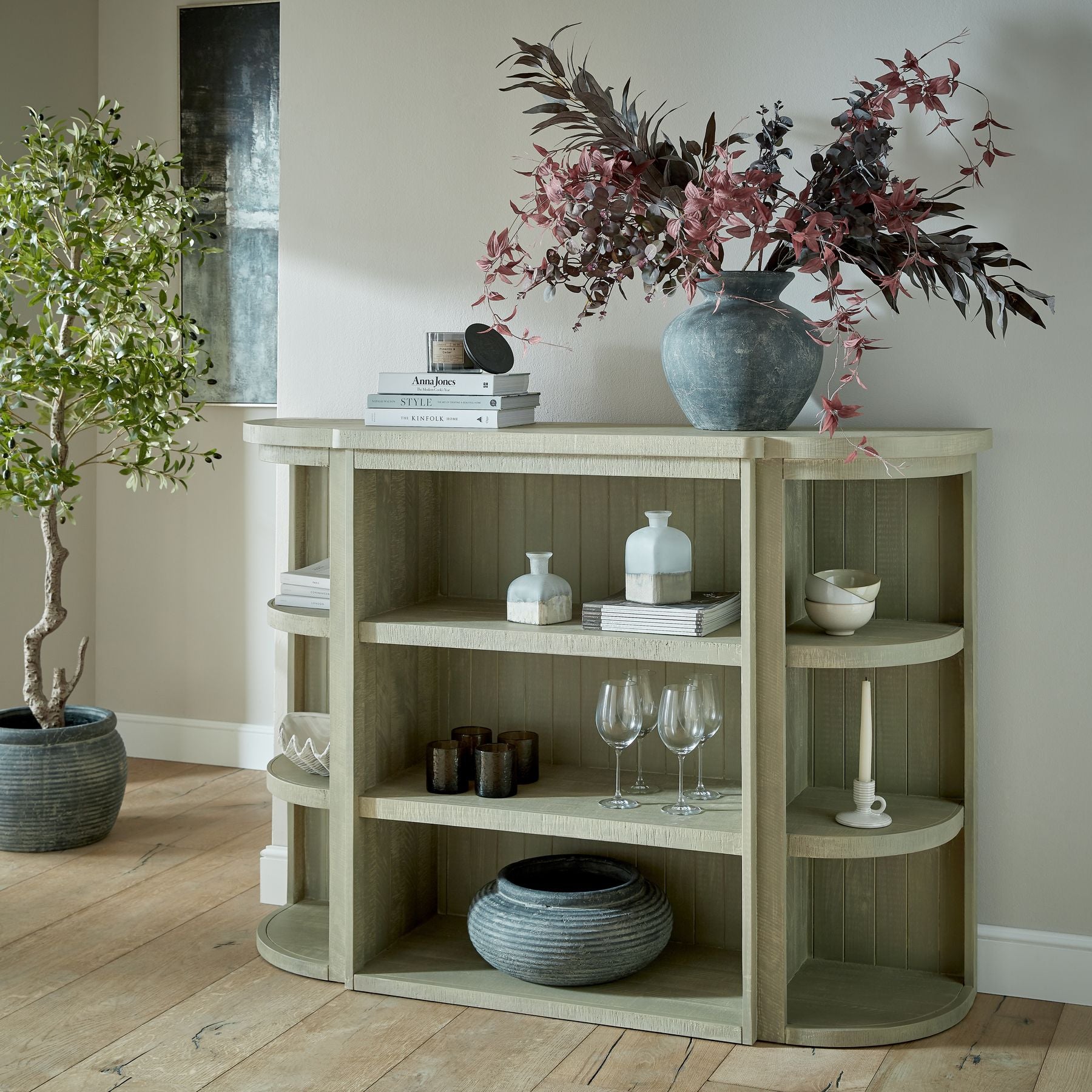 Wooden shelf with decorative items including a vase with flowers, books, and vases on a wooden floor.
