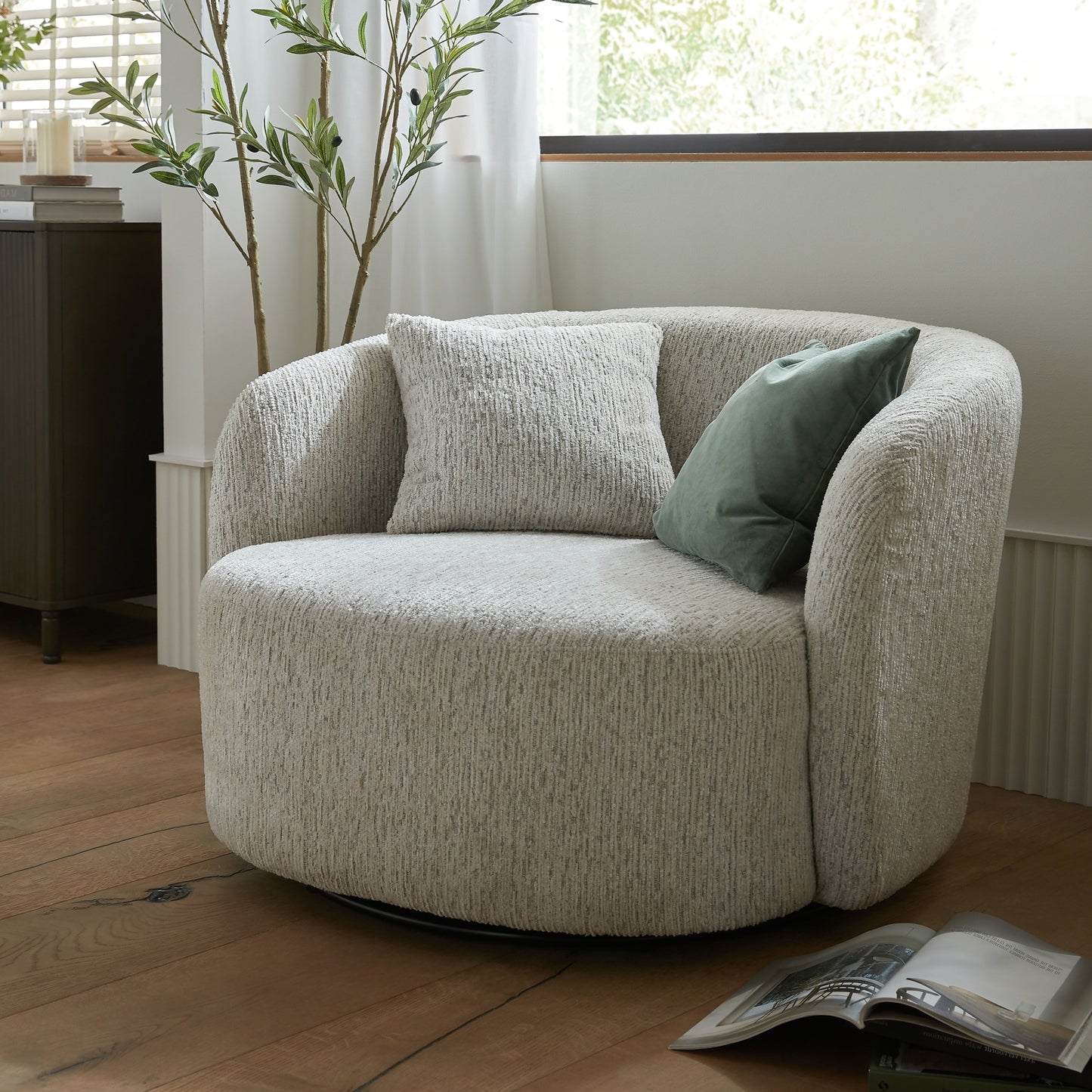 Beige armchair with green pillow in a room with wooden floor and plant