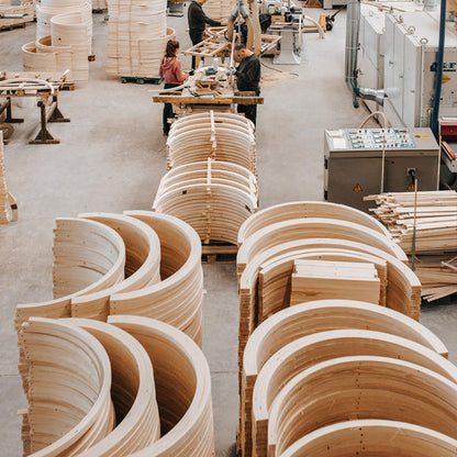 Wooden curved panels in a factory setting with workers in the background