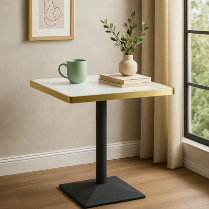 Small table with a green mug, books, and a plant in a room with a window and wall art.