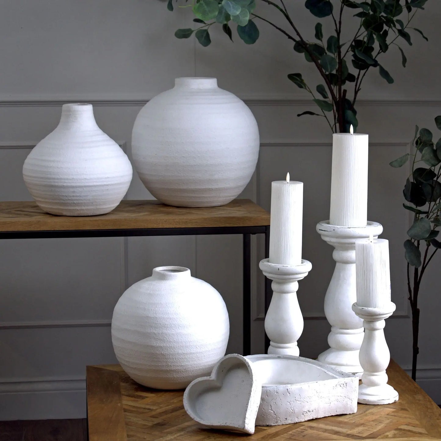 White ceramic vases and candle holders on a wooden surface with a neutral background